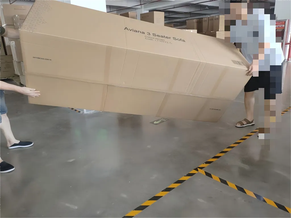 Two workers handling a packed sofa carton during drop-test inspection